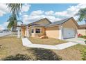Charming tan home featuring a two-car garage, a well-maintained lawn, and a beautiful blue sky at 115 Anzio Dr, Kissimmee, FL 34758