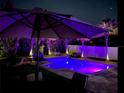 Backyard view of a swimming pool at night, illuminated with colorful lights, surrounded by palm trees and a white fence at 14963 Yorkshire Run Dr, Orlando, FL 32828