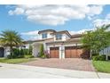 Charming two-story home with a three-car garage, complemented by lush landscaping and a beautiful brick driveway under a blue sky at 13136 Alderley Drive Dr, Orlando, FL 32832