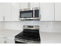 Close-up of stainless steel microwave and electric range with white subway tile backsplash at 1027 Cloud Ridge Ct, Mount Dora, FL 32757