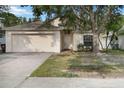 Beige single-Gathering home with a two-car garage and a tidy front lawn with mature tree shading the facade at 3370 Cypress Point Cir, St Cloud, FL 34772