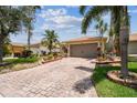 Home showcasing a brick driveway leading to a two-car garage, with lush landscaping and mature trees at 608 Grand Canal Dr, Poinciana, FL 34759