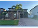 Inviting two-story home boasts stone detailing, a brick driveway, and vibrant tropical landscaping at 3159 Somerset Park Dr, Orlando, FL 32824