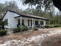 Exterior view of a single-story home with columns, covered front porch, and black Adirondack chairs and mature trees at 8310 Happy Trails, Kissimmee, FL 34747