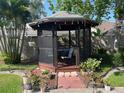 Screened gazebo, furnished with a table and chair, surrounded by beautiful plants and a brick walkway at 4926 Reginald Rd, Orlando, FL 32829