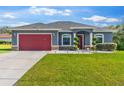 Well-maintained one-story home with a lush green lawn and a red garage door at 3292 Sw 133Rd Lane Rd, Ocala, FL 34473