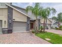 Attractive townhome featuring a two-car garage, brick driveway, and lush tropical landscaping at 783 Ocean Course Ave, Davenport, FL 33896