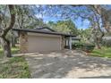 Paved driveway and a two-car garage with stone accents beneath mature trees at 9905 Nicoma Ln, Orlando, FL 32817