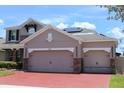 Three car garage with red brick driveway, stone accents, solar panels, and taupe paint at 2805 Carter Grove Ln, Kissimmee, FL 34741