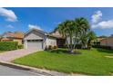 Charming home featuring a well-manicured lawn, palm trees, and a brick driveway leading to a two-car garage at 4056 Ashton Club Dr, Lake Wales, FL 33859