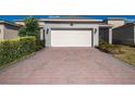 Wide driveway with a two-car garage featuring a brick-paved driveway and manicured landscaping at 11051 Bostwick Aly, Winter Garden, FL 34787