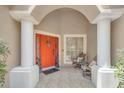 Welcoming front porch with tiled flooring, columns, and an bright orange entry door at 651 Regina Cir, Oakland, FL 34787