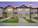Exterior dusk shot of a new townhome featuring attached garages, well-manicured lawns, and sidewalk at 816 Longboat Dr, Davenport, FL 33896