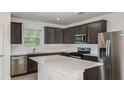 Modern kitchen features stainless steel appliances, dark wood cabinets, a white countertop island, and tiled floors at 9076 Wildlight Trl, Wildwood, FL 34785
