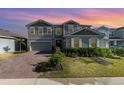 Charming two-story home with a manicured lawn, brick driveway, and beautiful sunset sky at 3200 Canna Lily Pl, Clermont, FL 34711