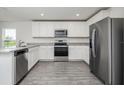 Modern kitchen with white cabinets, stainless steel appliances, granite countertops, and gray wood-look flooring at 409 Ashbury Way, Poinciana, FL 34759