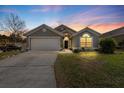 Dusk view of a single-story home featuring an attached two car garage and manicured lawn at 112 Thorne Meadow Pass, Davenport, FL 33897
