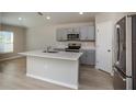Open kitchen with island, stainless appliances, and wood-look floors; bright, modern design at 1570 Sage Ave, Haines City, FL 33844