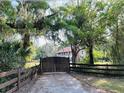 View of the gated driveway leading to the two-story home with a red roof surrounded by lush trees at 18700 Ravenswood Rd, Altoona, FL 32702
