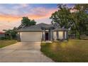 Home at sunset with gray exterior, stone accents, white garage door, and manicured front lawn at 12164 Se 85Th Ct, Belleview, FL 34420