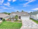 Beautiful single-Gathering home featuring a well-manicured lawn, mature landscaping, and a decorative patterned driveway at 1709 Latta Ct, The Villages, FL 32162