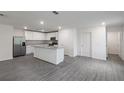 Open kitchen with island, stainless steel appliances, and modern gray wood flooring at 575 Bay Leaf Dr, Poinciana, FL 34759
