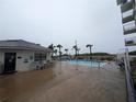 Outdoor pool area with lounge chairs, palm trees and building's exterior under a cloudy sky at 3100 Ocean Shore Blvd # 101, Ormond Beach, FL 32176