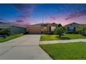 Single-story home with a manicured lawn, tan exterior, and attached two-car garage at dusk at 2612 Canyon Crest Dr, Lakeland, FL 33811
