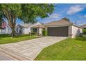 Long paver driveway leading to an attached garage, complemented by lush green lawn and mature shade trees at 9345 Se 171St Le Flore Ln, The Villages, FL 32162
