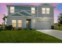 Two-story home with gray and blue siding, white trim, and a two-car garage, set on a green lawn at dusk at 1424 Axel Cir, Winter Haven, FL 33880