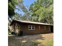 Rear view of a single-story home surrounded by mature trees, featuring a metal roof and neat landscaping at 2748 Cr 543, Sumterville, FL 33585
