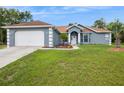 Front view of a one-story gray home featuring a two car garage, a well-manicured lawn and mature trees at 8628 Sw 133Rd Lane Rd, Ocala, FL 34473