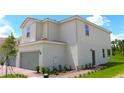 Side view of a two-story home featuring a two-car garage, manicured landscaping and a red brick walkway at 584 Bay Leaf Dr, Poinciana, FL 34759