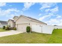 Side view of a beige home featuring well-maintained lawn, two-car garage, and a white fence at 887 Galloway St, Lake Alfred, FL 33850