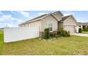 Side view of a beige home showing manicured lawn, white fence, and partial view of the garage at 887 Galloway St, Lake Alfred, FL 33850