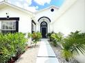 Welcoming entryway with a black front door, white stone pathway, and lush tropical landscaping at 132 Canary Island Cir, Davenport, FL 33837