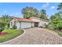 Single-story home with a tile roof, a brick driveway, an attached garage, and lush landscaping at 509 Osprey Ln, Winter Springs, FL 32708