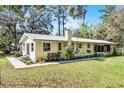 Back of the single-story home with mature trees, well-kept lawn, and a glimpse of the screened porch at 53722 Rivertrace Rd, Astor, FL 32102