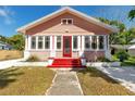 Charming pink house featuring a red front door, surrounded by green lawn and white trim at 205 Mary Ave, New Smyrna Beach, FL 32168