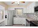 Well-lit kitchen featuring stainless steel refrigerator, mosaic tile backsplash, and white cabinetry at 3005 Garden Rd, Eustis, FL 32726