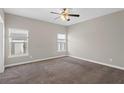 A carpeted room featuring neutral walls and a ceiling fan, bathed in natural light from two windows at 303 Puffer Ct, Kissimmee, FL 34759
