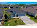Aerial view of a well-maintained home with a gray exterior, paver driveway, lush lawn, and beautifully landscaped surroundings at 418 Aquamarine Way, Daytona Beach, FL 32124