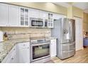 A modern kitchen featuring granite countertops, stainless steel appliances, and white cabinets with glass fronts, with a door to another room at 4670 Links Village Dr # B102, Ponce Inlet, FL 32127