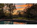 Backyard view of an in-ground pool with iron fencing, and a beautiful sunset with orange and yellow hues at 150 Lake Charles Rd, Deland, FL 32724
