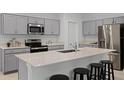 Modern kitchen features sleek stainless steel appliances, gray cabinets, an island with bar seating, and quartz countertops at 2743 Gentle Rain Dr, Davenport, FL 33837