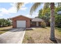 Charming brick home featuring a one-car garage, concrete driveway, and tropical landscaping at 2126 Sabal Palm Dr, Edgewater, FL 32141