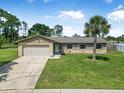 Charming single-story home featuring a lush green lawn, a palm tree, and an attached garage at 1191 Tracy Dr, Port Orange, FL 32129