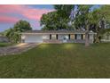 Charming one-story home with brick facade, attached garage, and a lush green lawn under a colorful sky at 2106 Umbrella Tree Dr, Edgewater, FL 32141