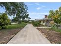 Long concrete driveway leading to a well-kept yellow home with mature landscaping and a brick chimney at 1411 Cliff Ave, Eustis, FL 32726