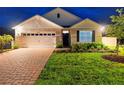 Charming single-story home at night featuring a well-manicured lawn, brick driveway at 33436 Shutterfly Way, Sorrento, FL 32776